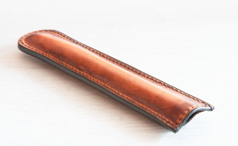 May include: A brown leather pen case with a stitched edge.