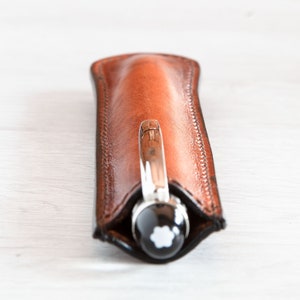 May include: A brown leather pen case with a silver pen inside. The pen has a black cap with a white star logo.