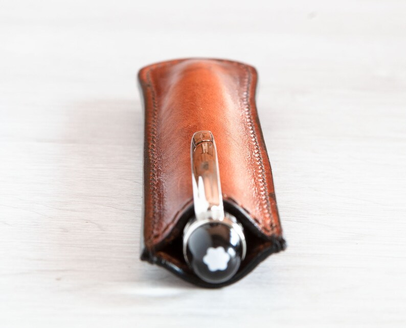 May include: A brown leather pen case with a silver pen inside. The pen has a black cap with a white star logo.