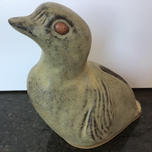 May include: A ceramic duck ornament in green and brown hues. The duck features a textured surface, a brown eye, and wing detailing. This decorative figurine is designed to be a charming home decor item.