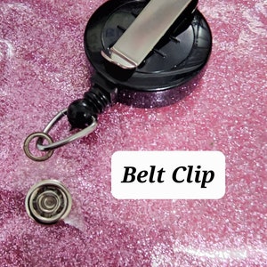 May include: A black retractable badge holder with a silver belt clip. The holder has a spring-loaded reel and a swivel hook.