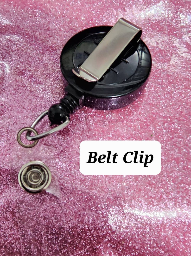 May include: A black retractable badge holder with a silver belt clip. The holder has a spring-loaded reel and a swivel hook.