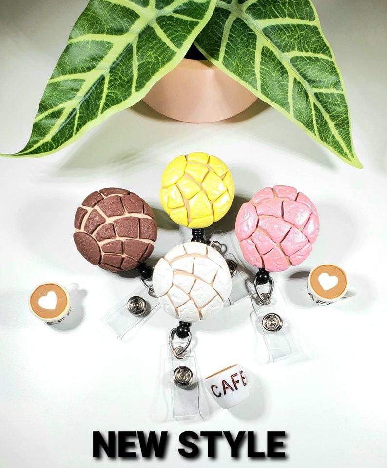 May include: Four colorful, round, bread-shaped charms with a textured surface, attached to retractable badge holders with clear plastic ID card holders. The charms are brown, yellow, pink, and white.  The badge holders also include a small charm of a coffee cup with the word "CAFE" on it.  The text "NEW STYLE" is at the bottom of the image.