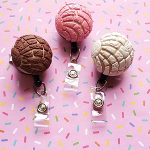 May include: Three colorful, round, pastry-shaped badge holders with a white background. The badge holders are pink and white, brown and white, and white.