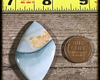 May include: A light blue, white, and orange agate cabochon with a diamond shape. The cabochon is about the size of a US penny.