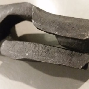 May include: Close-up of a black metal tool with a textured surface. The tool has a handle and a jaw with a small opening.