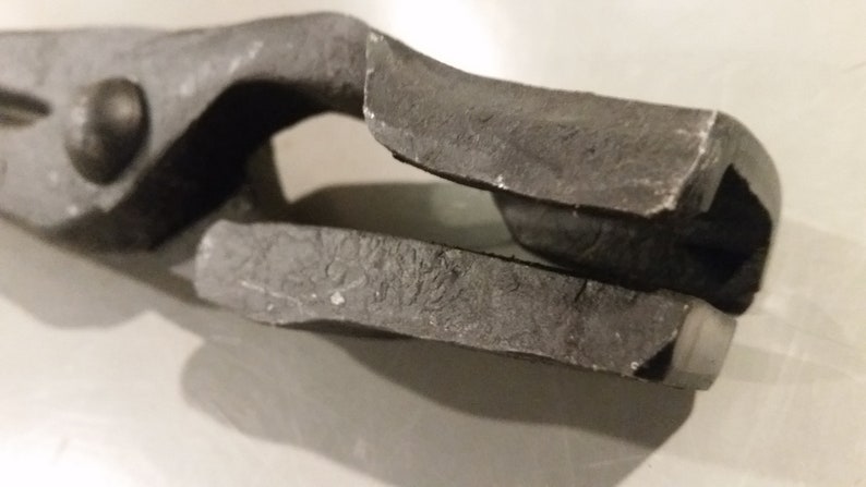 May include: Close-up of a black metal tool with a textured surface. The tool has a handle and a jaw with a small opening.