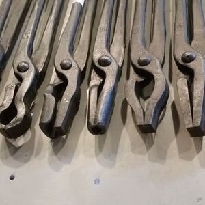 May include: A set of ten blacksmith tongs with various jaw shapes and sizes. The tongs are made of metal and have a dark gray finish.