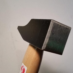 Könnte beinhalten: Ein schwarzer Hammer mit einem Holzstiel. Der Hammerkopf hat eine quadratische Form mit einer leicht gebogenen Fläche.