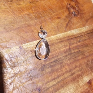 May include: A clear glass teardrop-shaped crystal pendant with a smaller, faceted crystal at the top. The crystal is attached to a silver wire.