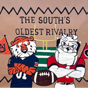 May include: A brown poster with the text "THE SOUTH'S OLDEST RIVALRY" and illustrations of a tiger and a bulldog, representing Auburn and Georgia. The tiger holds an orange flag with "AU" on it, and the bulldog holds a red flag with a "G".