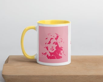 Puede incluir: Una taza de cerámica blanca con interior y asa rosas, con un retrato rosa de una mujer con cabello rubio sobre un fondo rosa. La taza está sobre una superficie de madera. El asa y el interior son amarillos.