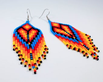 May include: A pair of long, beaded earrings with a geometric pattern in shades of blue, orange, yellow, and black. The earrings are made of small, colourful beads and have a fringe-like design.