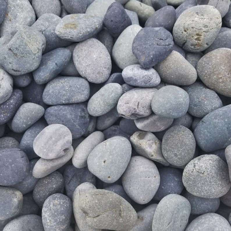 May include: A collection of smooth, grey and black river rocks. The rocks are various sizes and shapes, and they are arranged in a close-up view.