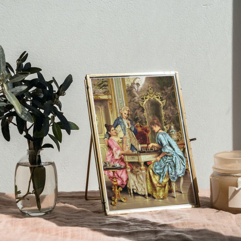 Rococo chess players print in a frame leaning against the wall beside a plant; frame not included.