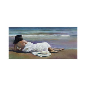 May include: A woman in a white dress lies on a sandy beach, facing the sea. She has a white sun hat next to her.