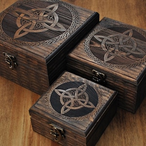 Op de afbeelding: Drie houten kisten van verschillende afmetingen, met een Keltisch knoopontwerp dat in de deksels is gesneden. De kisten zijn donkerbruin gebeitst en hebben metalen sluitingen. De Keltische knoop is omgeven door een cirkelvormige rand.