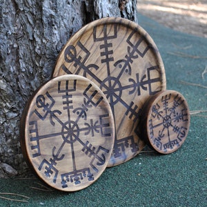May include: A set of four wooden decorative trays with a dark brown finish. Each tray features a carved Vegvisir symbol, a Viking compass believed to guide the bearer. The trays vary in size, with the largest approximately 12 inches in diameter.