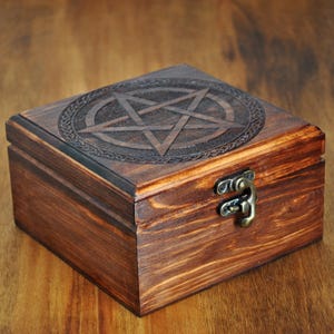 May include: A wooden box with a carved pentagram design on the lid. The box has a brass latch and is made of dark wood.