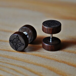 May include: A pair of wooden ear gauges with a dark brown finish. One gauge features a carved Celtic knot design.