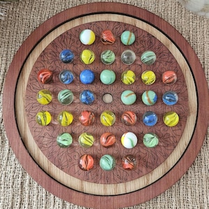 May include: A wooden game board with a mandala design and 24 colorful glass marbles. The marbles are arranged in a circle around the center of the board.