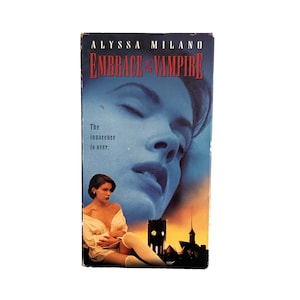 Puede incluir: Cinta de VHS de la película "Embrace of the Vampire" con Alyssa Milano. La portada presenta el rostro de una mujer en tonos azules, con el título en rojo. Una segunda imagen muestra a una mujer con un vestido blanco y calcetines altos.