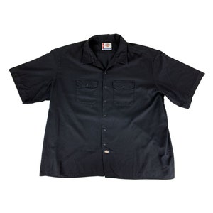 May include: A black short-sleeved button-down shirt with two chest pockets and a brand label on the left side of the collar.