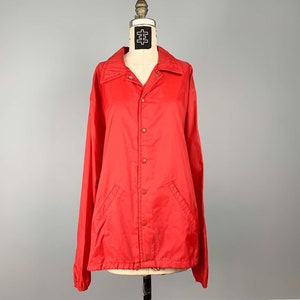 Op de afbeelding: Een licht rood jack met knopen en lange mouwen.