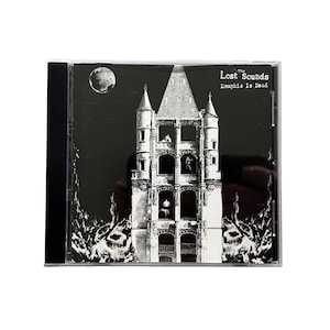 Op de afbeelding: Een cd-hoesje met een zwart-witte albumhoes. De illustratie toont een kasteel met figuren in de ramen, een maan en de tekst "The Lost Sounds Memphis Is Dead."
