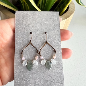 May include: A pair of dangle earrings with a delicate wire frame and a mix of light pink, white, and green gemstone beads.