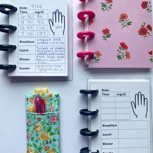 May include: A collection of small notebooks and a pen holder. The notebooks have clear plastic covers and are bound with black and pink rings. One notebook has a floral cover. The notebooks contain handwritten data and charts.