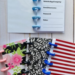 Puede incluir: Una colección de mini cuadernos con varias cubiertas, incluyendo patrones florales, a rayas y de hojas. Los cuadernos están encuadernados con anillos de plástico de colores y tienen páginas rayadas para notas. Un cuaderno está abierto, mostrando campos para fecha, sitio web, correo electrónico, contraseña y notas.