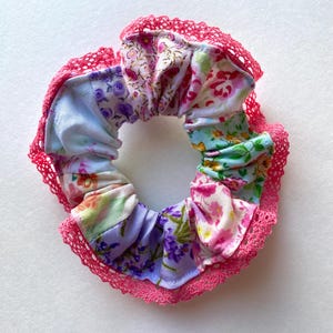 Puede incluir: Un scrunchie de tela floral rosa y blanca con un borde de encaje rosa.