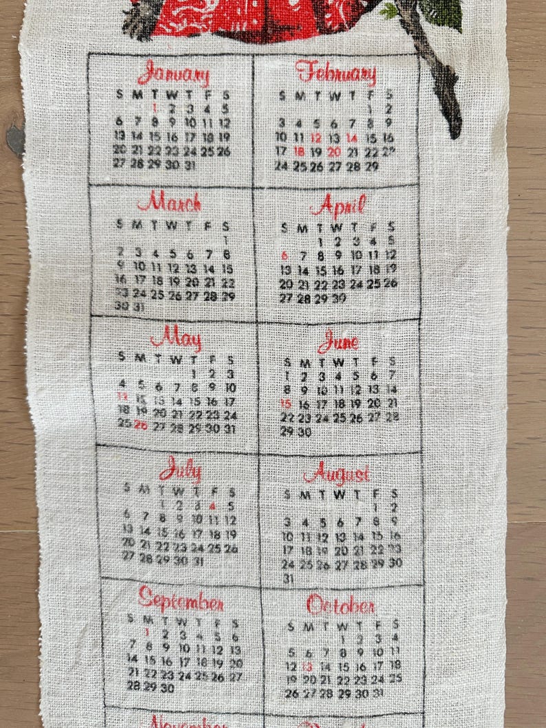 May include: A vintage calendar printed on a cream-colored fabric. The calendar displays the months from January to October, with each month's name in a decorative script. The days of the week and dates are printed in black.