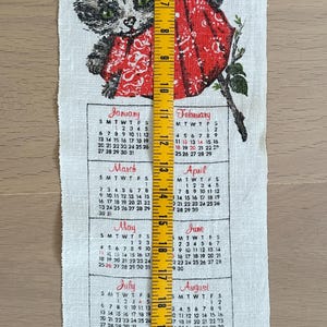 May include: A white linen calendar towel featuring a gray cat wearing a red scarf, with a 1930 calendar. The towel is approximately 26 inches long, with months and dates printed below the cat illustration.