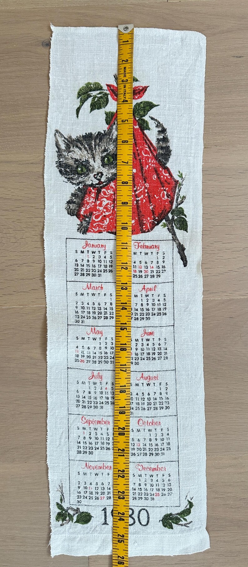 May include: A white linen calendar towel featuring a gray cat wearing a red scarf, with a 1930 calendar. The towel is approximately 26 inches long, with months and dates printed below the cat illustration.