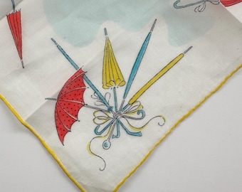Op de afbeelding: Witte zakdoek met een gele rand, met een patroon van rode, gele en blauwe paraplu's. De paraplu's zijn gerangschikt met strikken en wolkvormige vormen, wat een vintage esthetiek creëert.