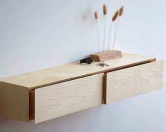 Puede incluir: Estantería flotante de madera clara con dos cajones, montada en una pared blanca. La estantería está decorada con un pequeño bloque de madera que sostiene plantas secas, un reloj negro y un juego de llaves. La estantería mide unos 100 cm de largo.