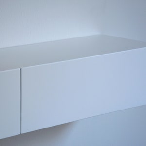 May include: A white floating shelf with two compartments. The shelf is mounted on a white wall.