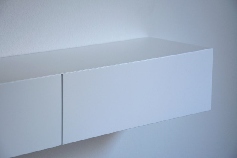 May include: A white floating shelf with two compartments. The shelf is mounted on a white wall.