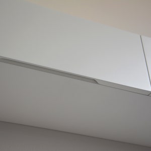 May include: White kitchen cabinets with a recessed handle.
