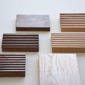 May include: An assortment of wooden soap dishes in various shades of brown and natural wood. Some have a grooved design, while others are smooth. The arrangement showcases the different textures and colors of the wood.