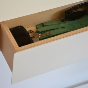 May include: A white drawer with a wooden trim is open, revealing a black wallet, a set of keys, a pair of green gloves, and a pair of brown sunglasses.