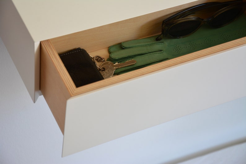 May include: A white drawer with a wooden trim is open, revealing a black wallet, a set of keys, a pair of green gloves, and a pair of brown sunglasses.