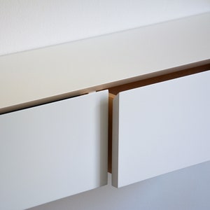 May include: White wall-mounted cabinet with two drawers, one open and one closed. The drawers have a simple, modern design.