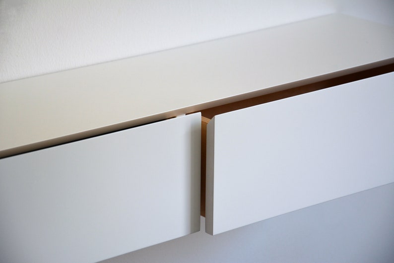 May include: White wall-mounted cabinet with two drawers, one open and one closed. The drawers have a simple, modern design.