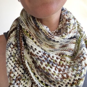 May include: A white, brown, green, and gray knitted scarf with a lacy pattern.