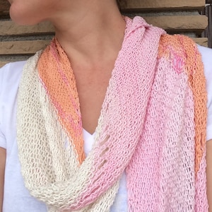 May include: A soft, knitted scarf in shades of pink, peach, and cream. The scarf is made of a lightweight yarn and has a delicate, open-weave texture.