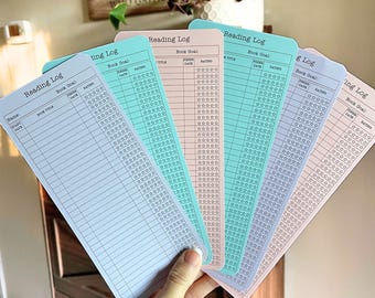 May include: A hand holds a fan of five pastel-colored reading log cards. Each card has a header that reads "Reading Log" and includes sections for book title, date, and rating. The cards are in shades of blue, pink, and green.
