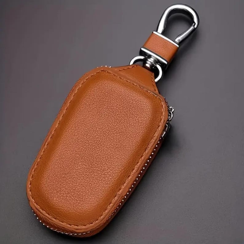 Puede incluir: Un llavero de cuero marr&oacute;n con una bolsa con cremallera y un gancho de metal plateado.